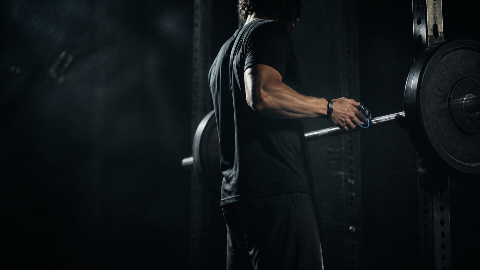 An athlete attaching a small sensor to a barbell in a squat rack